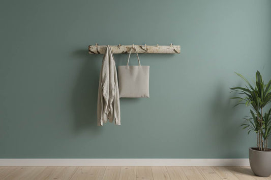 Eine Garderobe aus Birkenstamm mit Haken aus Holz mit verschiedenen Kleidungsstücken an einer grünen Wand. 