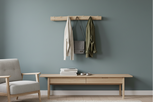 Eine Garderobe aus Birkenstamm mit Haken aus Holz mit verschiedenen Kleidungsstücken an einer grünen Wand. 